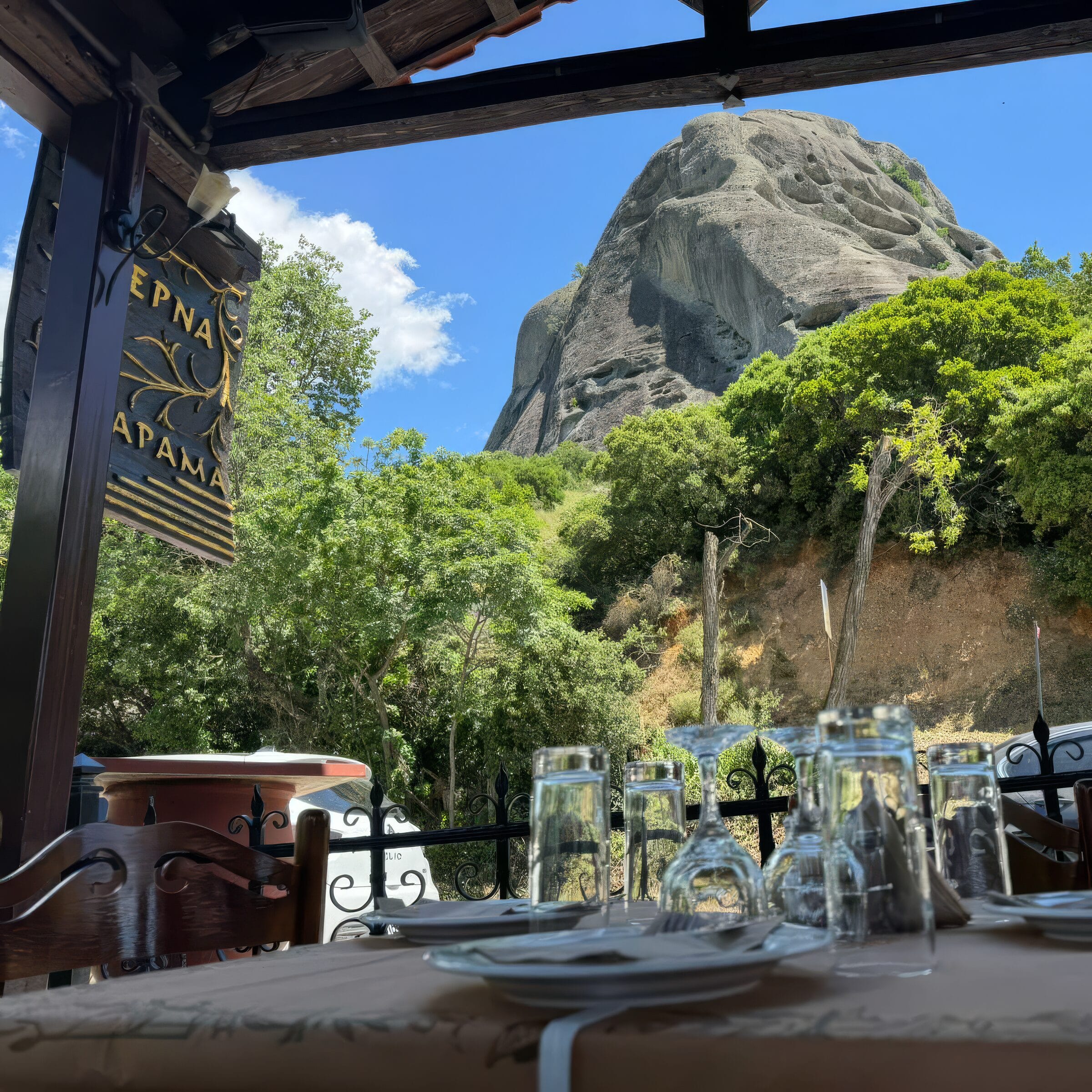 The shaded terrace of Taverna Xarama with a laid table, looking out to a towering Meteora rock in Kastraki